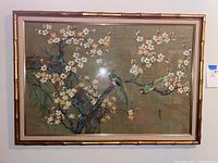 Front view of framed Asian inspired artwork showing two green birds and flowering branches.