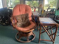 Full view of the vintage bamboo swivel chair with coral cushion and leopard print throw pillow, alongside the rectangular bamboo side table.