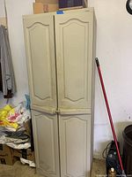 Front view of the tall beige plastic cabinet with four paneled doors, showing exterior condition.