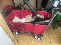Red collapsible wagon containing an Echo handheld leaf blower and fabric collection bag, shown inside a wooden shed.