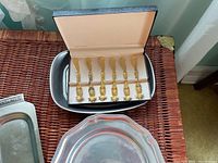 Box of 6 gold plated hors d'oeuvre spreaders shown on top of stainless plate and decorative silver bowl.