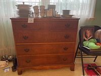 Front view of wood dresser with four drawers and metal handles, showing the full piece with light from window behind.