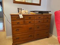 Front view of wood dresser showing 10 drawers with metal handles, top surface laden with personal items not included.
