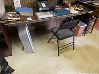 Photo showing the folding table positioned against a wall with various items placed on it, and the black folding chair underneath.