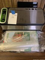 Front view of FoodSaver vacuum sealer with bags and manual included underneath it.