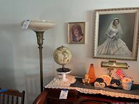Floor lamp and decorative items on piano top including globe, metronome, wooden cat, and music mug with pencils.