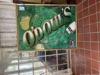 Large framed O'Doul's picture, green background with logo, behind glass, hung on wall near doorway.
