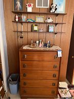 Full view of dresser with 5 drawers and wall-mounted wooden shelves above holding assorted decor