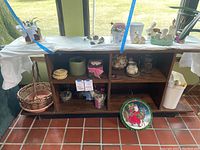 Shelf and table with various planting decor including planters, glass containers with sea shells, rattan coasters, figurines, and a Santa Claus hanger plate.