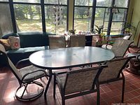Wide view of outdoor table and six chairs arranged around it in sunroom environment.