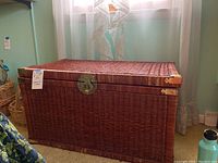 Front view of vintage rattan chest showing overall rectangular shape, reddish-brown woven material, and metal lock center front.