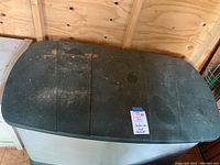 Closed Rubbermaid outdoor storage container showing green lid with some dirt and sticker on top