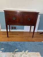 Front view of solid wood buffet showing two cabinet doors with oval metal handles, carved decorative details on legs and doors.