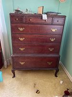 Front view of a solid wood dresser showing multiple drawers with brass handles and decorative carved details at the edges and legs.