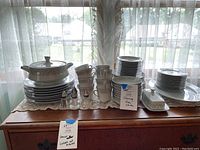 Full view of Sterling Fine China set arranged on wooden dresser including plates, cups, saucers, serving bowl with lid, serving plate, butter dish, and two salt and pepper shakers.
