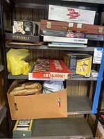 Three shelves filled with vintage board games such as Scrabble, Ungame, Dominoes, and some sports equipment like a baseball glove in a box.