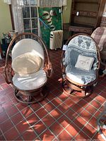 Photo showing both bamboo swivel chairs with cushions and pillows in sunroom with tiled floor and surrounding furniture.