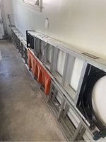 Two aluminum ladders laid flat in a garage: a long extension ladder and a shorter step ladder visible underneath.