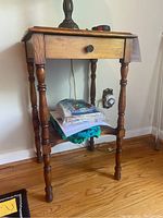 Front and right side view of one vintage end table showing drawer with knob, turned spindle legs, and lower shelf with fabric items removed.