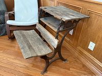 Side and seat angle view of antique wrought iron and wood school desk showing fold-down seating and wooden desk surface.