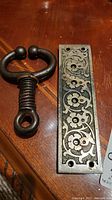 Photo showing the antique iron bull nose ring and the decorative steel lock mechanism plate on a wooden surface.
