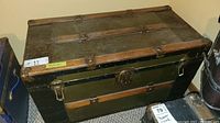 Full view of antique steamer trunk showing black exterior with wood slats and metal buckles.