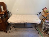 Front-facing photo of the wrought iron bench with fabric-covered foam cushion showing decorative curved armrests and the foam cushion covering with floral pattern.