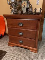 Front view of the wood chest of drawers showing three closed drawers with metal semi-circular pull handles and visible wood grain finish.