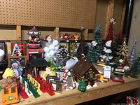 Overview of tabletop featuring ceramic houses, Mickey Mouse train station, boxed musical carousel, pine cones, picture frames, and assorted Christmas figurines and decorations.