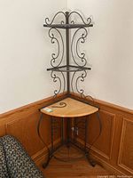 Full view of metal corner rack with three metal shelves and one wooden shelf at bottom, showing scroll metal design.