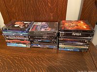 Two stacks of DVDs showing various titles including movies, documentaries, sports and music DVD cases arranged on a wooden surface