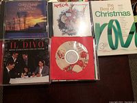 Photo showing a group of eight Christmas music CDs displayed on a table, including Il Divo - The Christmas Collection, Christmas Country, The Best of Christmas, and a CD with a festive Santa Claus-themed cover.