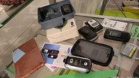 Photo of three flip phones and related accessories displayed on glass with labels and boxes