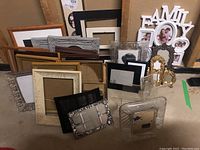 Wide view showing a variety of picture frames in different colors, materials, and sizes including wood, plastic, and metal. Some frames have glass or matte inserts.