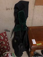 Black golf bag standing upright, showing green velvet padded head cover and shoulder straps.