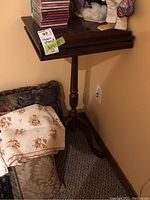 Wooden music stand with rectangular surface, some scrapes visible, standing next to furniture and textiles in a carpeted room.