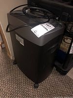 Side view of the Royal brand black and gray paper shredder with cord visible and one broken caster on the bottom