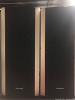 Front view of two black Pioneer speakers with vertical silver accent strips on the grilles, showing the Pioneer logo at bottom center.