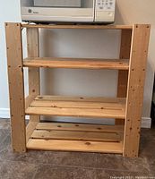 Front view of solid pine storage shelf showing four slatted wooden shelves with a microwave on top (not included).