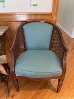Front view showing wood frame, caned sides, and blue upholstered seat and backrest with cushion