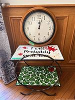 Front view of the clock mounted above the wrought iron side table showing both decorative shelves.