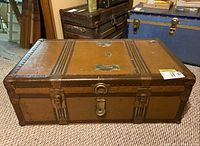 Closed view of vintage metal steamer trunk showing brown exterior, metal clasps, reinforcements, and vintage Zellers labels on top surface.