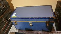 Closed blue vintage steamer trunk with brass hinges and metal corner protectors.