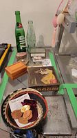 Overview photo showing all items on the table including vintage pop bottles, various trinket boxes and telephone wire art in a basket.