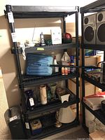 Black resin shelving unit with 5 shelves, photographed filled with unrelated items to show scale and structure. Unit is lightweight and appears modular for easy disassembly.