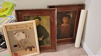 Three prints leaning against a wall including two large framed portraits and one smaller unframed floral print.