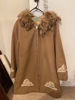 Front view of tan wool parka with fur-trimmed hood and appliqué igloo details on sleeves and lower front.