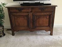 Front view of the antique wooden sideboard showing two drawers and two doors with metal handles.