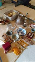 Photo of various bowls, lamp parts, candle holders, carved wooden plaques, and other decorative items arranged on carpet.