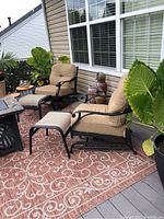 Two metal rocking chairs with beige cushions and two matching foot stools on outdoor rug